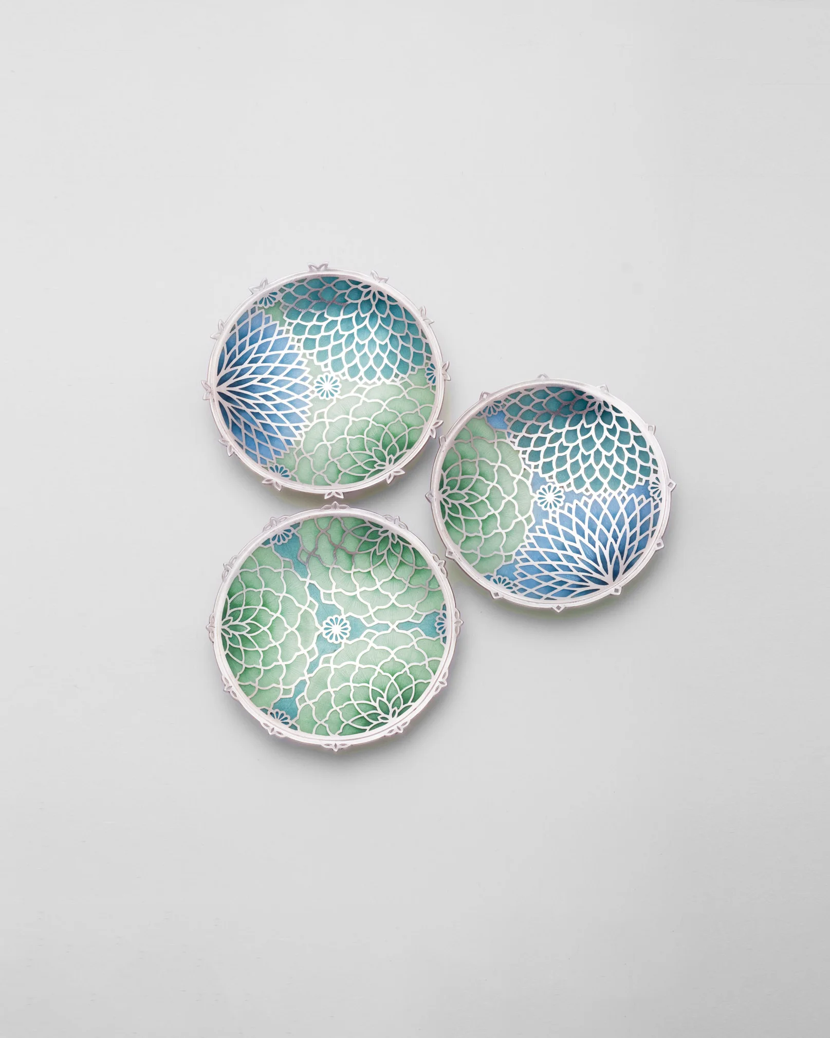 Three circular pieces with delicate silver-coloured patterns over blue and green.